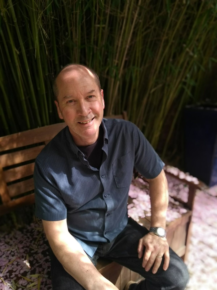 Photo image of historian Stephen Brumwell sitting on a garden bench, smiling.